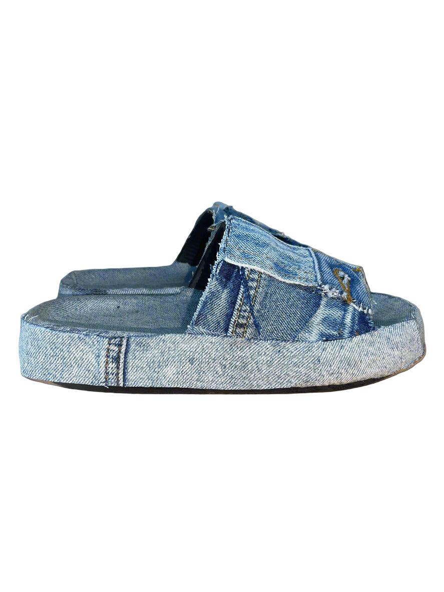 A pair of blue denim slides with a platform sole, placed against a neutral background.